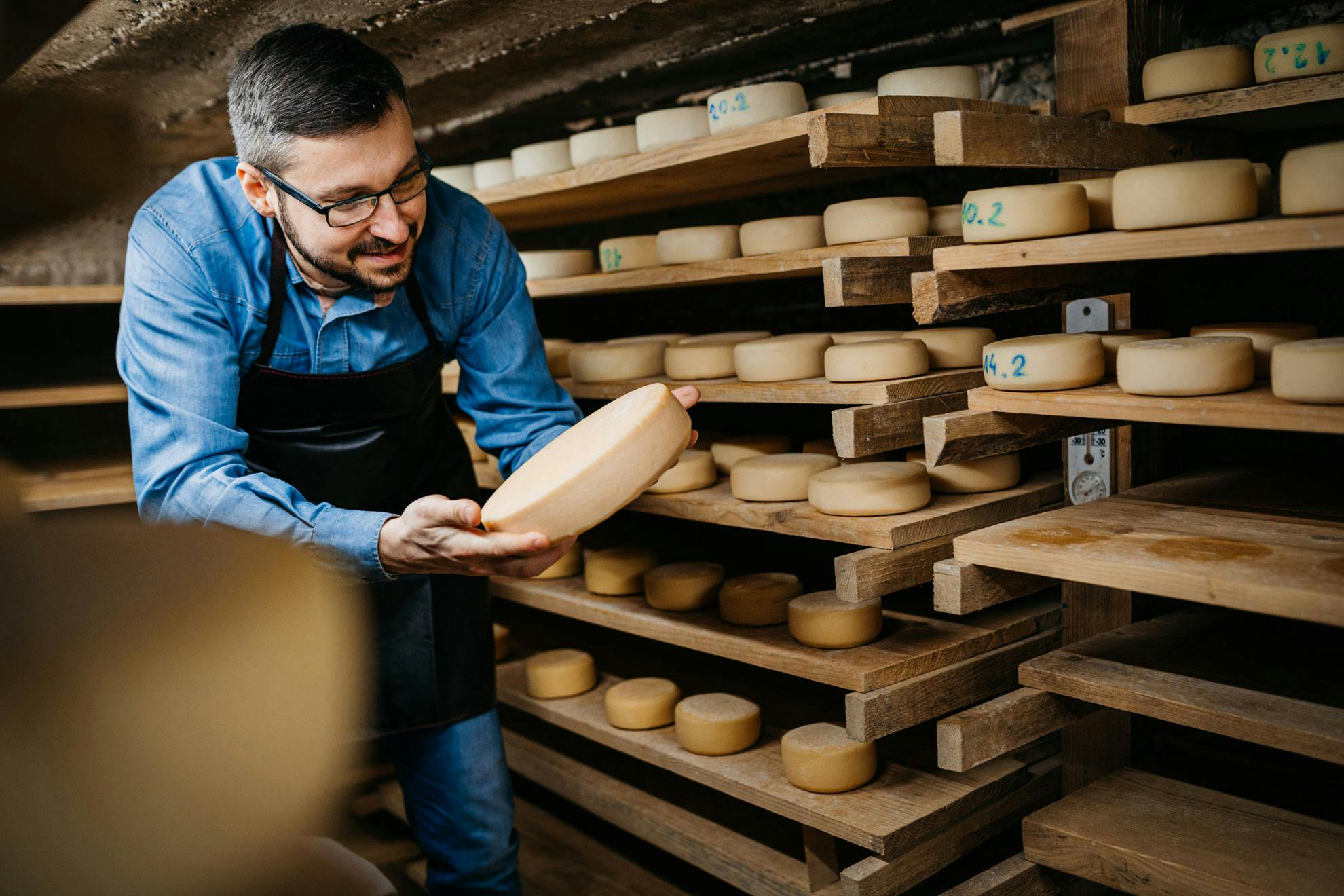 Käsemeister mit Käse vor Regalen voller Käse